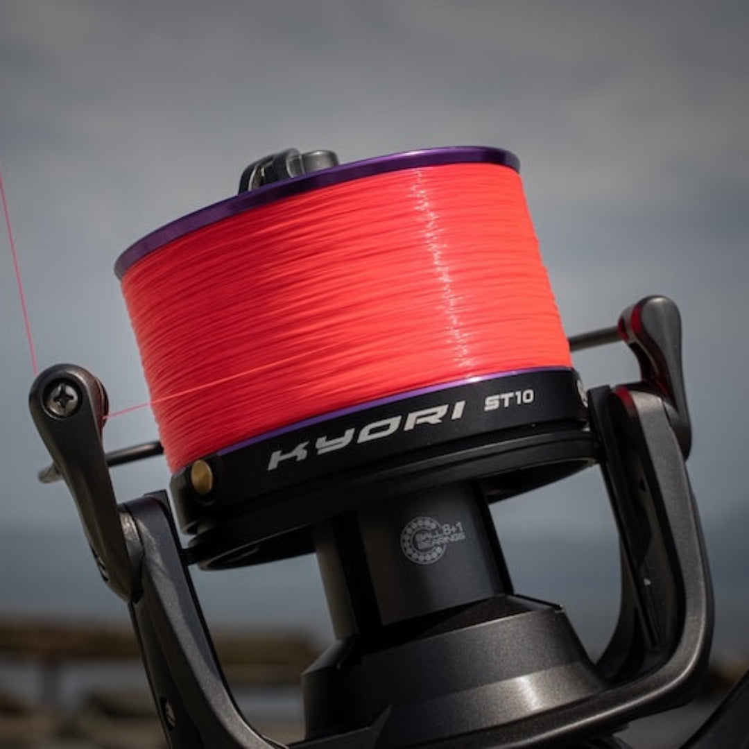 Fishing reel with red line spool on a blurred natural background