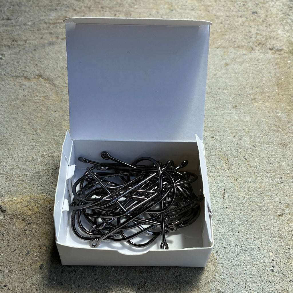 Bulk Box of black fishing hooks on a concrete surface