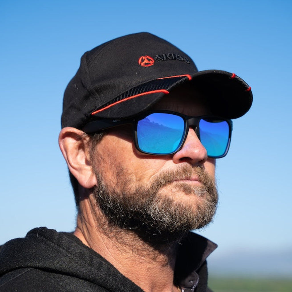 Man wearing a black cap and sunglasses with a clear blue sky background
