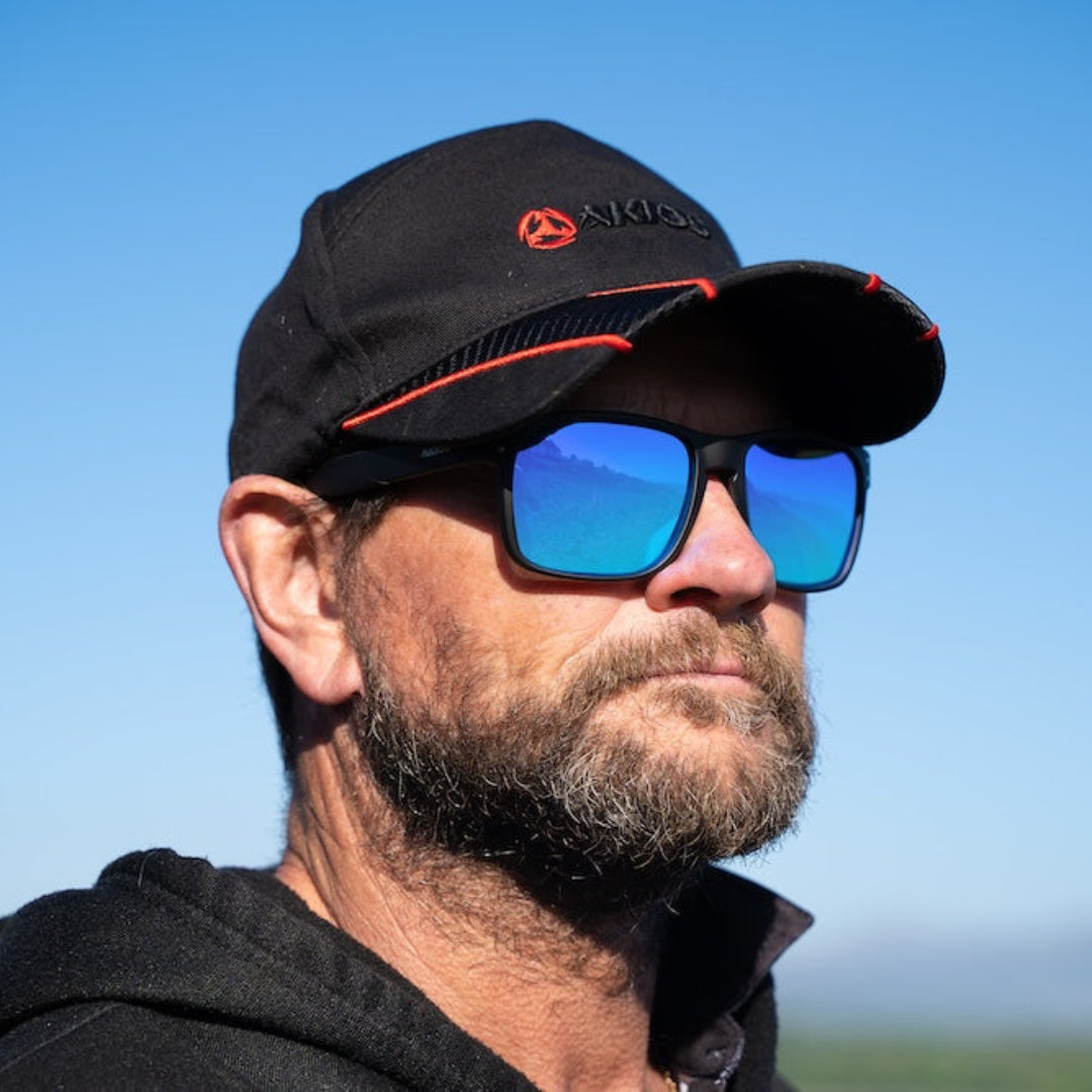 Man wearing a black cap and sunglasses with a clear blue sky background