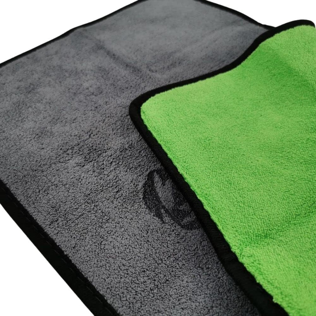 A close-up of a gray microfiber cloth with a black border, showing its textured surface and a bright green reverse side with black trim.