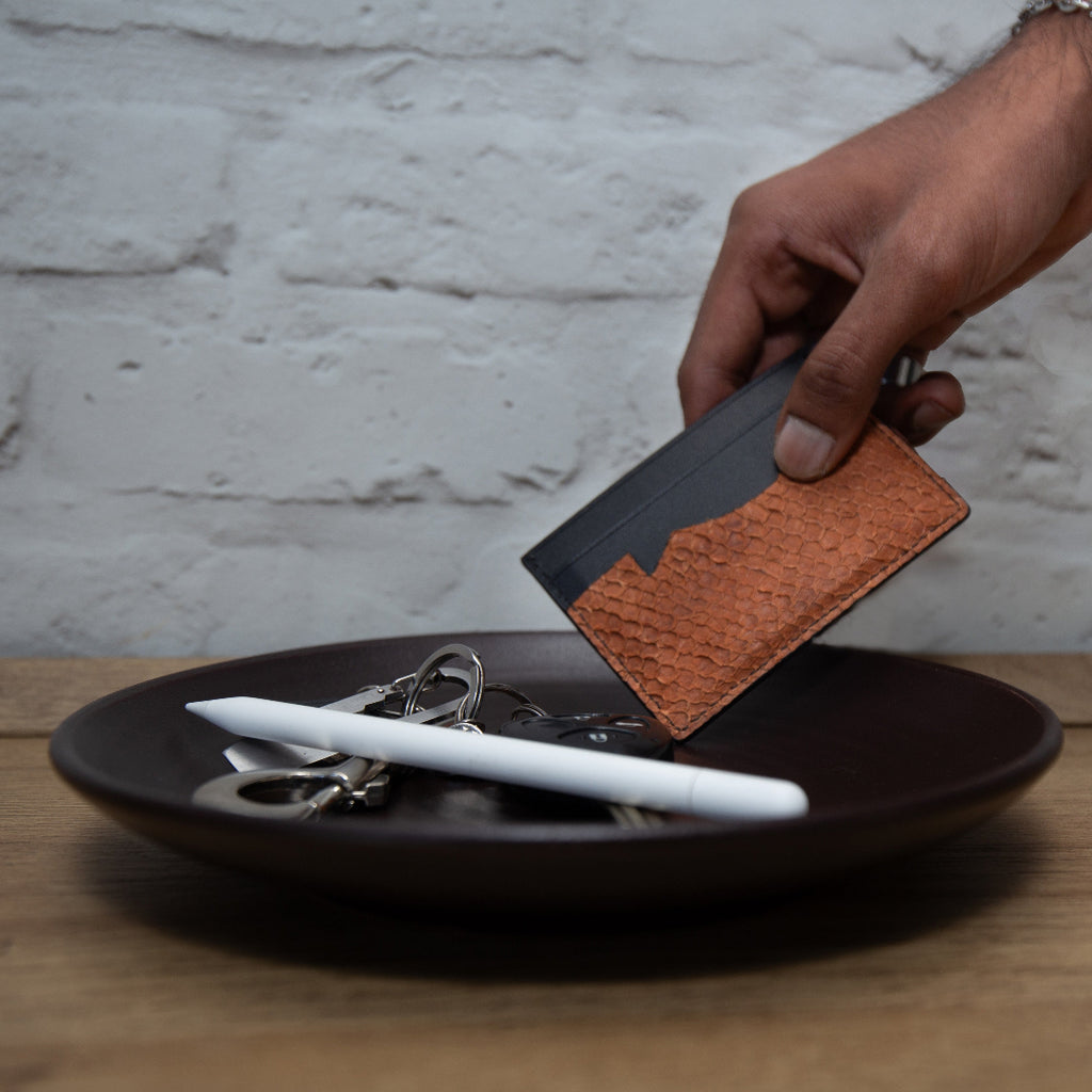 Person holding a ofishal fish leather card wallet with a brown leather patch over a plate with keys