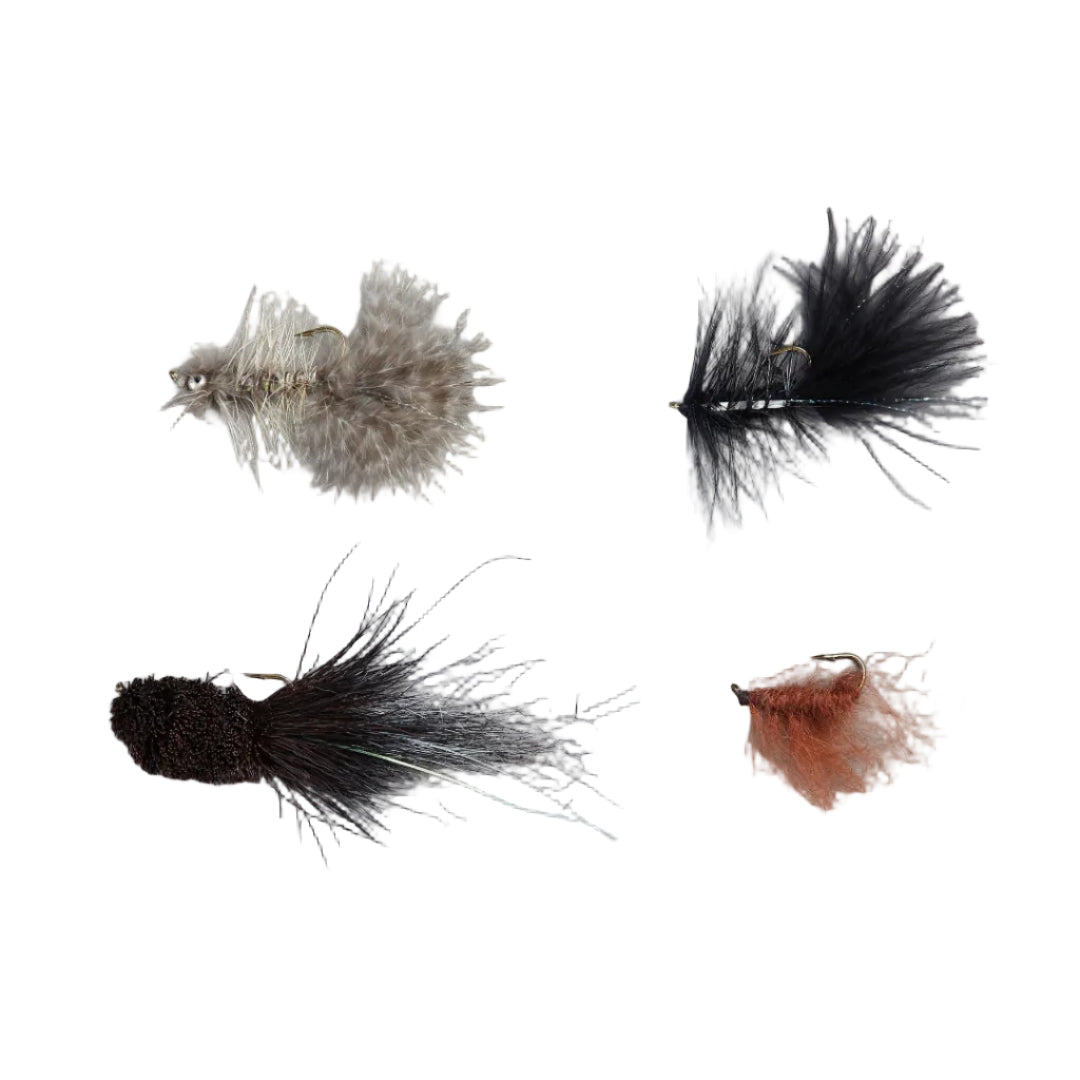 Four fly fishing lures arranged on a light gray background: a beige and brown feathered fly, a black hackle with white striping, a dark brown and black nymph-style fly, and a small orange-and-brown nymph fly.