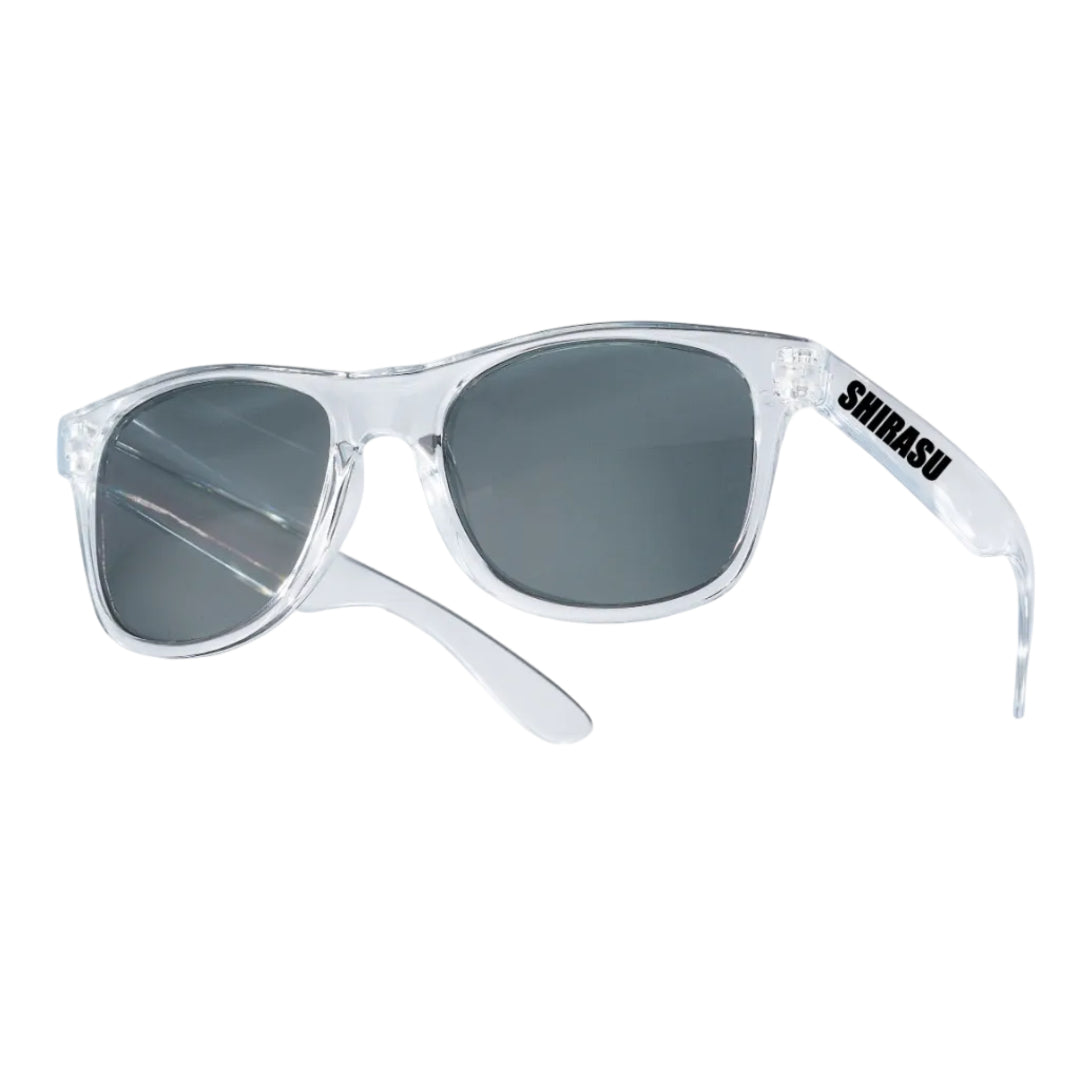Clear acetate sunglasses with dark gray lenses and a black 'SHIRASU' logo on the temple arm, shown on a solid white background.